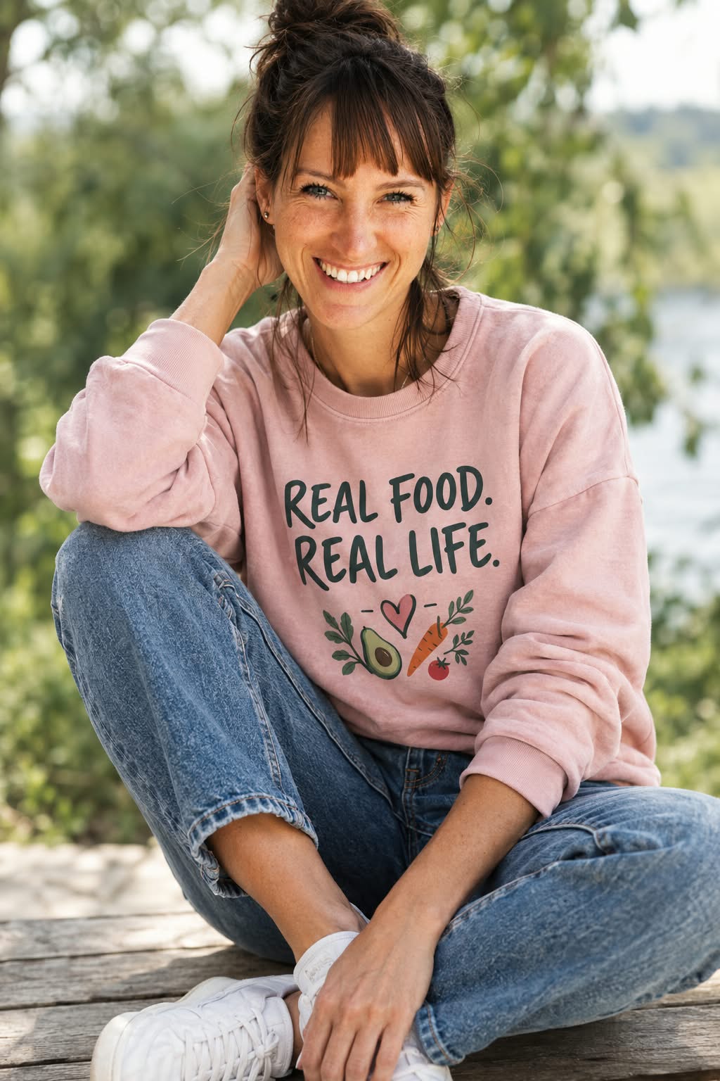 Yvonne Borzym lacht in die Kamera, sie sitzt im Grünen und trägt einen rosa Pullover mit der Aufschrift Real Food. Real Life.